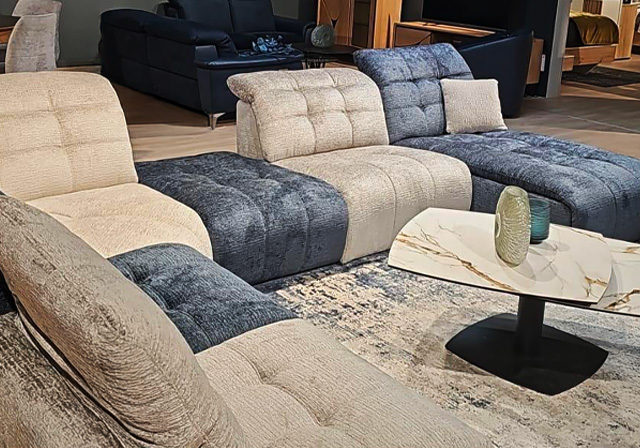 Canapé modulable contemporain en tissu beige et bleu nuit, avec assise large et dossiers réglables, présenté sur un tapis design avec table basse en céramique blanche marbrée