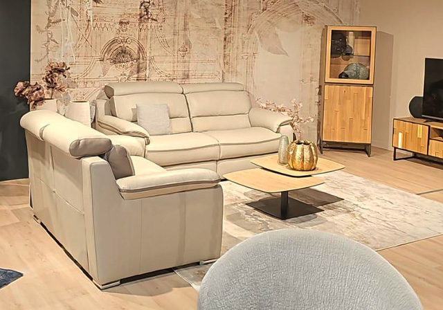 Salon moderne avec canapé en cuir crème, fauteuil assorti et table basse carrée en bois clair, dans un intérieur chaleureux au décor mural artistique